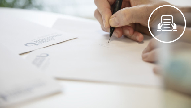 Hand somhåller i en penna och skriver på ett papper.