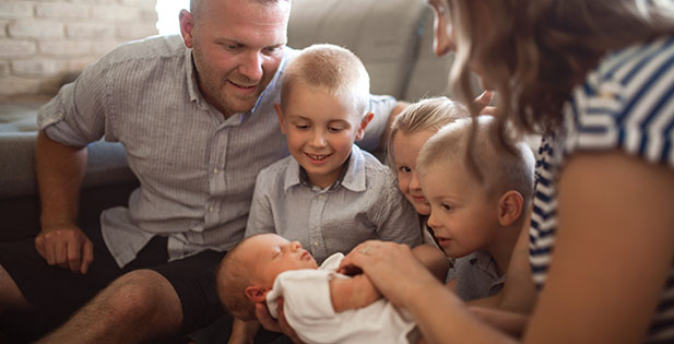 Mor, far och tre syskon tittar på en nyfödd baby