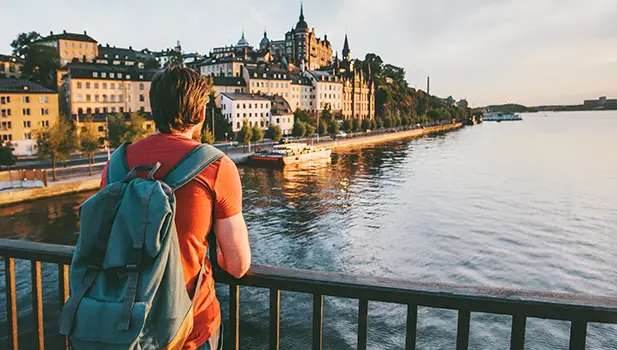 Ung man med ryggsäck står på en bro och blickar över Riddarfjärden i Stockholm